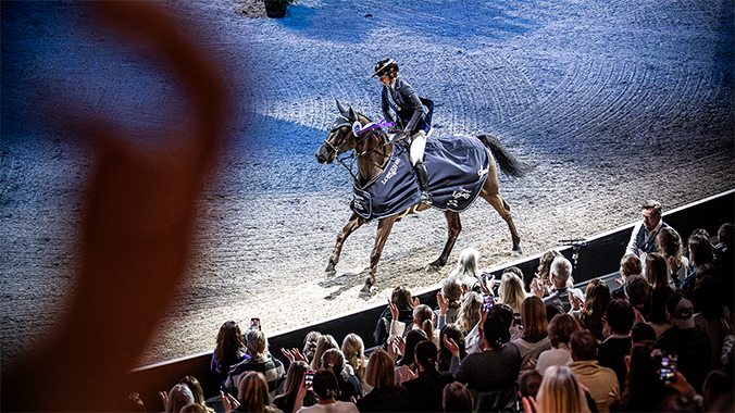 Ryttare och häst galopperar förbi läktare med människor i vinsttäcke.